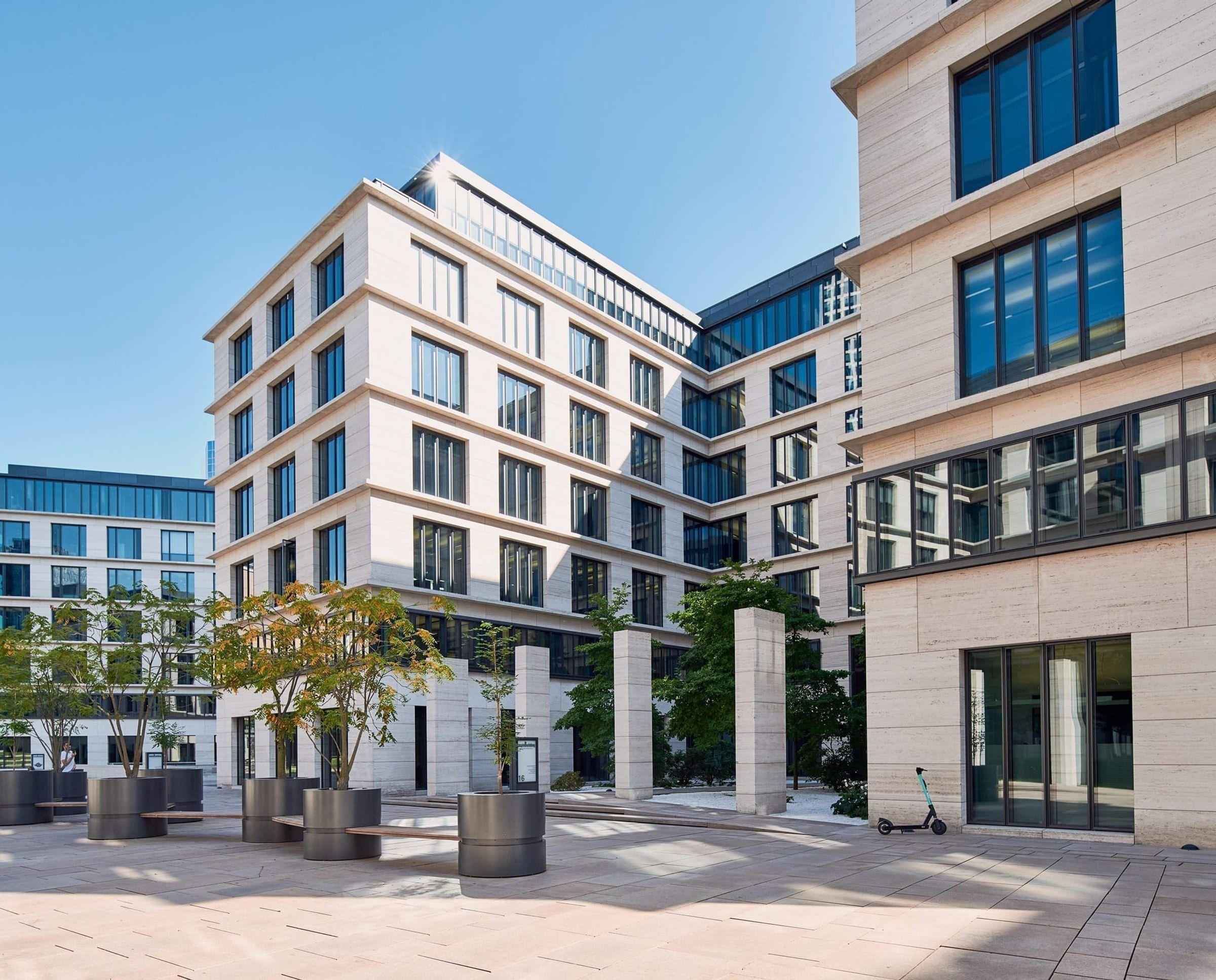 Architecturally appealing office complex with a mixture of glass and stone structures. The open courtyard area is designed with trees, seating and geometric columns.
